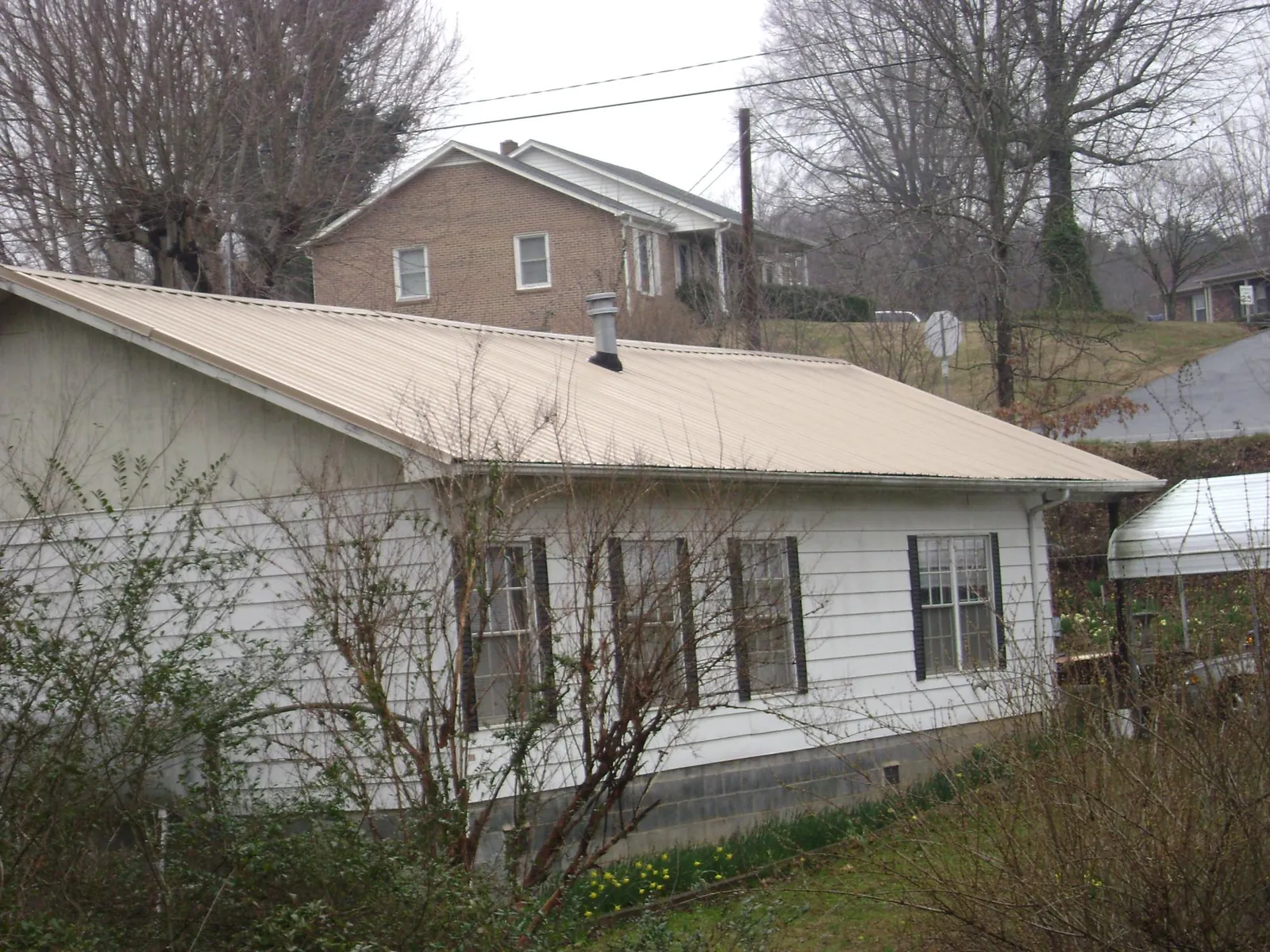 Tan metal roof on a white sided house set into a hillside — Commercial Roofing by Roofing Brothers in Pine Valley